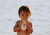 Repas de bébé en voyage : un bébé boit son biberon à la plage pendant les vacances d'été
