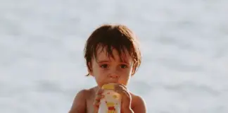 Repas de bébé en voyage : un bébé boit son biberon à la plage pendant les vacances d'été
